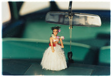 Load image into Gallery viewer, Photograph by Richard Heeps.  A hula doll sits on a dashboard, below the rear view mirror.  The car&#39;s interior is green and out of focus.