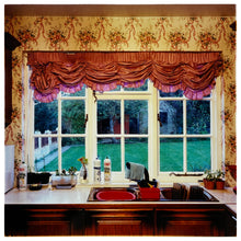 Load image into Gallery viewer, Photograph by Richard Heeps. A kitchen sink from 1989 with brown taps and bowl, and surrounded by three bottles of washing up liquid.  The window above the sink looks out on a neat garden and is topped with orange ruched curtains.  The wallpaper has a sequence of orange flowers linked with orange ribbon.  