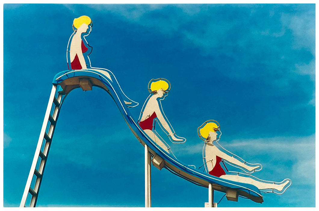 Three females on a slide on a neon sign against a blue sky with clouds photograph by Richard Heeps.
