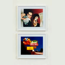 Load image into Gallery viewer, A couple look into the camera in burlesque costume against a red wall. Contemporary portrait photography by Richard Heeps framed in white
