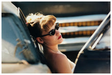 Load image into Gallery viewer, Photograph by Richard Heeps.  A woman rests on the side of a car.