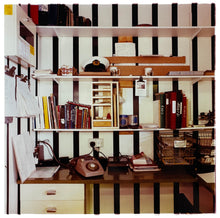 Load image into Gallery viewer, A photograph from the 1980s, an office with filled shelves which are fixed on bold black and white striped wallpaper. Photograph by Richard Heeps