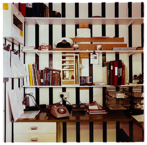 A photograph from the 1980s, an office with filled shelves which are fixed on bold black and white striped wallpaper. Photograph by Richard Heeps