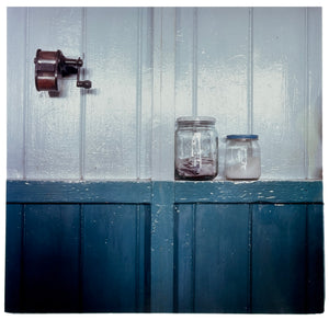 Photograph by Richard Heeps. A pencil sharpener is attached to the white part of a two-tone wall. Halfway down the wall turns blue and here is a shelf providing a narrow home to two screw-top jars.