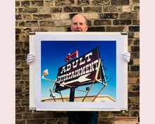 Load image into Gallery viewer, &#39;Adult Entertainment&#39; photographed in Beatty, Nevada, shows bold typography sitting prominently on an American road sign, against a background of bright blue sky. This fun and cheeky artwork was captured on a road trip through America and features in Richard Heeps&#39; sold out book &#39;Man&#39;s Ruin&#39;. An edition of this artwork recently sold at auction in The Auction Collective exhibition &#39;Hypercolor-Pop-Culture&#39;.