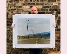 Load image into Gallery viewer, An open road in Amboy, California, featuring telephone poles disappearing into the mountainous distance. This classic and timeless landscape photograph is part of Richard Heeps&#39; &#39;Dream in Colour&#39; series. 