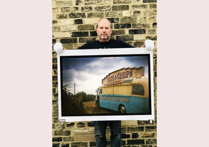 A moody Fenland sky is backdrop to a classic British Fish & Chips Van. The typography and the van itself has a fun fairground feel, contrary to the muted tones of this piece. Part of Richard Heeps series, 'A View of the Fens from the Car with Wings'.