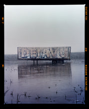 Load image into Gallery viewer, Photograph by Richard Heeps.  This photograph is tones of grey.  DEJAVU is painted on the side of a lorry trailer which sits in a grey watery fen, the sky is grey in the background. This photograph includes a film rebate.