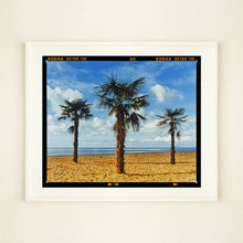 Load image into Gallery viewer, White framed photograph by Richard Heeps.  Three palm trees on the beach at Clacton-on-Sea with shadows cast by the early evening light.