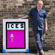 Load image into Gallery viewer, Photograph by Richard Heeps.  Richard Heeps holds a white framed print. At the top of the print, black letters spell out ICES and below is depicted a 99 icecream cone sitting left of centre against a pink coloured background.  