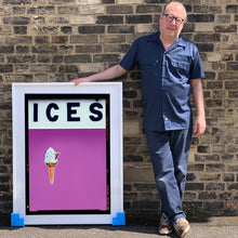 Load image into Gallery viewer, Photograph by Richard Heeps.  Richard Heeps holds a white framed print. At the top of the print, black letters spell out ICES and below is depicted a 99 icecream cone sitting left of centre against a plum coloured background.  