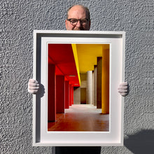 Load image into Gallery viewer, Monte Amiata housing, Gallaratese Quarter, Milan. Red and yellow brutalist architecture street photography by Richard Heeps framed in white.