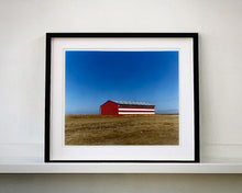 Load image into Gallery viewer, &#39;Stars &amp; Stripes Barn&#39; shows a depiction of the American flag painted on this isolated building in Oakhurst, California. It sits on the horizon against a vast bright blue sky. This artwork is part of Richard Heeps&#39; &#39;Dream in Colour&#39; series.