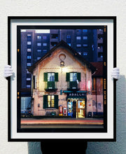 Load image into Gallery viewer, The traditional Italian Tobacconist shop, here in a Swiss Cottage style building set against a vast urban apartment block. 