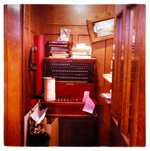 Load image into Gallery viewer, Photograph by Richard Heeps.  A wood panelled booth with an antique phone handset hanging on a hook on the left and an exchange in the middle, piled with books.