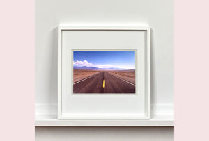 'The Road to Death Valley', taken in the Majove Desert, California, features a clouded blue sky met my mountains on the horizon. This American landscape artwork is part of Richard Heeps' 'Dream in Colour' series. Taken in 2001, this artwork was first executed in Richard's darkroom in 2021.