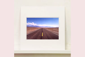 'The Road to Death Valley', taken in the Majove Desert, California, features a clouded blue sky met my mountains on the horizon. This American landscape artwork is part of Richard Heeps' 'Dream in Colour' series. Taken in 2001, this artwork was first executed in Richard's darkroom in 2021.