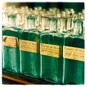 Photograph by Richard Heeps.  Rows of square green bottles labelled Tincture of Myrrh.