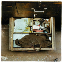Load image into Gallery viewer, Photograph by Richard Heeps.  The bottom drawer of a battered wooden work desk is open.  There is tobacco, a worn leather tool bag, a spool of string, scissors and other paraphernalia.