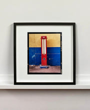 Load image into Gallery viewer, A red retro tyre pump against a yellow and blue painted wall, in the Porta Genova area of Milan. 