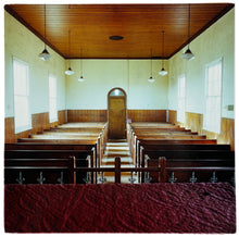 Load image into Gallery viewer, Photograph by Richard Heeps.  View of a small functional church from the purple pulpit cloth.  The pews are wooden and of basic design, the walls are painted white on the top half and wooden paneled on the bottom half.  Six basic pendular lights hang down from the wooden paneled ceiling.