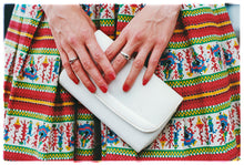 Load image into Gallery viewer, Photograph by Richard Heeps.  A white clutchbag, held by a pair of hands set against a vintage red patterned skirt.  