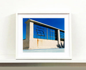 'Window of the World, Zzyzx Resort Pool', photographed in Soda Dry Lake, California shows window pains and a distressed wall, against a bright blue background of sky. This artwork is part of Richard's 'Dream in Colour' series. 