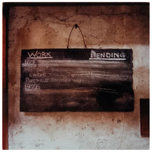 Load image into Gallery viewer, Photograph by Richard Heeps.  A chalk board with Work Pending written on the top with dates of 1976 and other chalk notes partially removed.  Chalk board hanging on a rough factory wall.