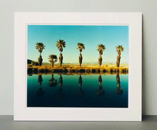 Load image into Gallery viewer, Plam trees stand tall against ombre skies in shades of blue and green in &#39;Zzyzx Resort Pool II&#39;, taken in Soda Dry Lake, California. This artwork was taken on a road trip from LA to Las Vegas. This photograph was taken on negative in 2002 but only executed in Richard&#39;s darkroom for the first time in 2017.